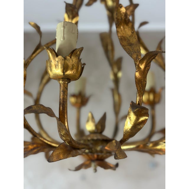 Elegant 1950s chandelier in gilded brass, featuring a finely crafted floral motif. Its airy design is composed of hammered...