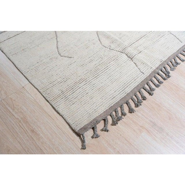 This hand knotted wool rug features a neutral color palette consisting of ivory, beige, cream, and white tones. Crafted in...