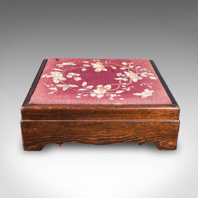 This is an antique upholstered footstool. An English, pitch pine fireside or lounge stool, dating to the Edwardian period,...