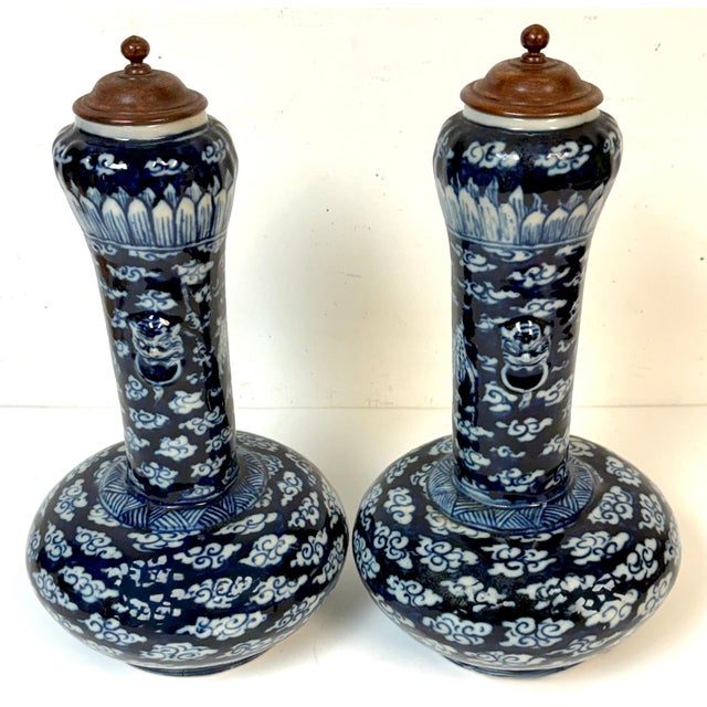 Pair of Late Qing Blue and White Porcelain Garlic-Neck Vases with Lion Mask Handles and Hardwood Covers A striking and...
