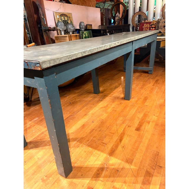 An impressive industrial work table covered in a weathered blue-grey painted base and a durable galvanized metal top. Its...