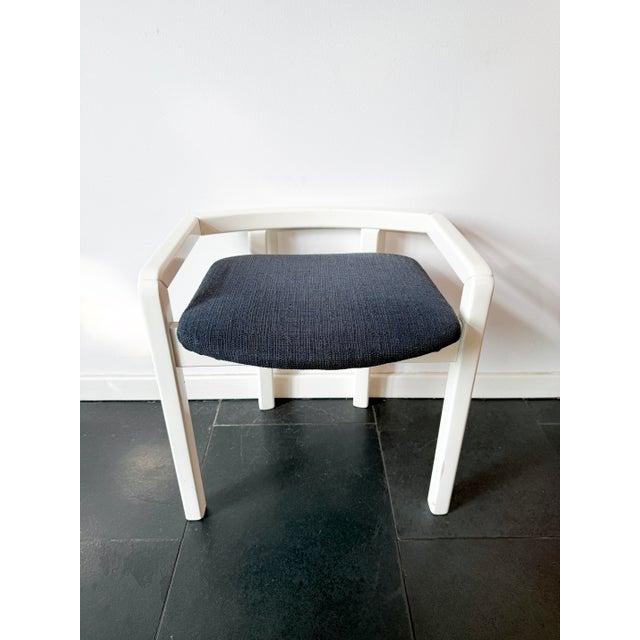 A vintage modernist wooden armchair with a white lacquered frame and a dark blue upholstered seat. The contrast between...