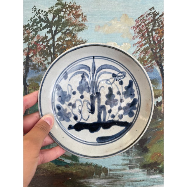 This likely antique ceramic dish features a hand-painted blue and white botanical motif rendered in fluid brushwork,...