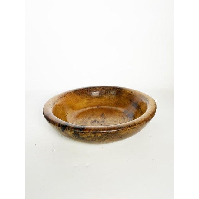 A beautiful artisanal bowl turned from a single piece of solid wood, showcasing stunning natural grain with warm shades of...