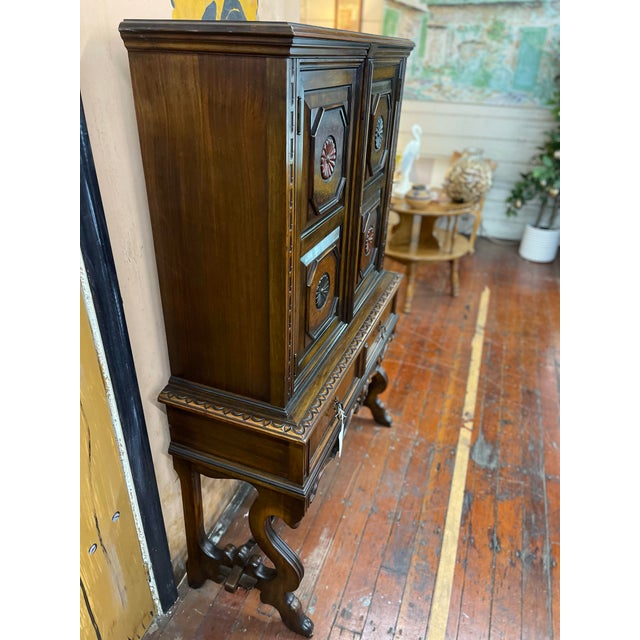 This tall, narrow cabinet features bold octagonal paneling with hand-painted rosette medallions, resting on an ornately...