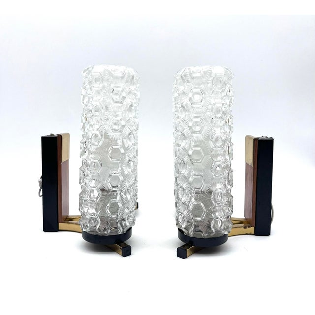 An elegant pair of mid-century wall lamps with striking cylindrical shades made of textured pressed glass. The decorative...