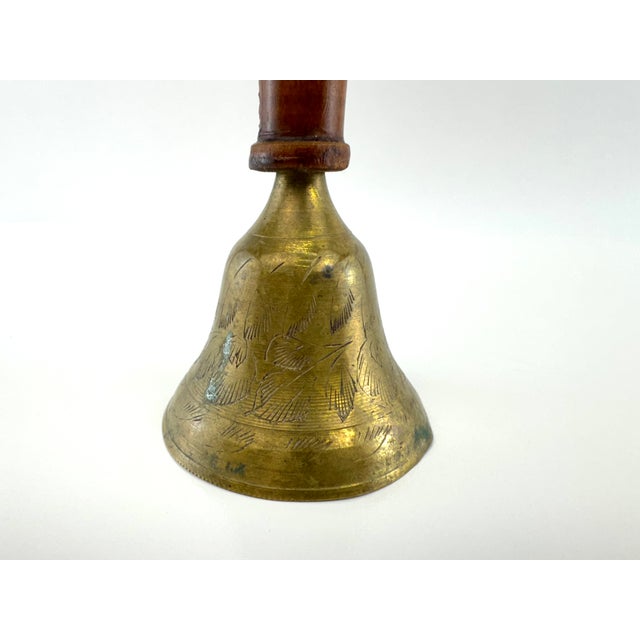 A vintage hand bell crafted with a warm turned wood handle and an engraved brass bell featuring hand-cut decorative...