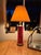 A striking vintage glass table lamp featuring a tall ruby red cylindrical body adorned with hand-painted gold leaf and...