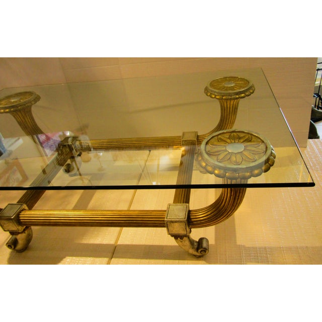 This Hollywood Regency Italian Silver and Gold Leaf Carved Wood and Glass Coffee Table is a stunning piece of furniture...