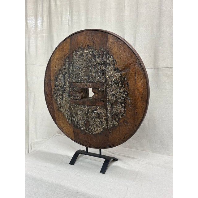 A commanding sculptural presence formed from an antique wooden ox cart wheel, mounted on a custom iron stand. The wheel’s...
