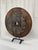 A commanding sculptural presence formed from an antique wooden ox cart wheel, mounted on a custom iron stand. The wheel’s...