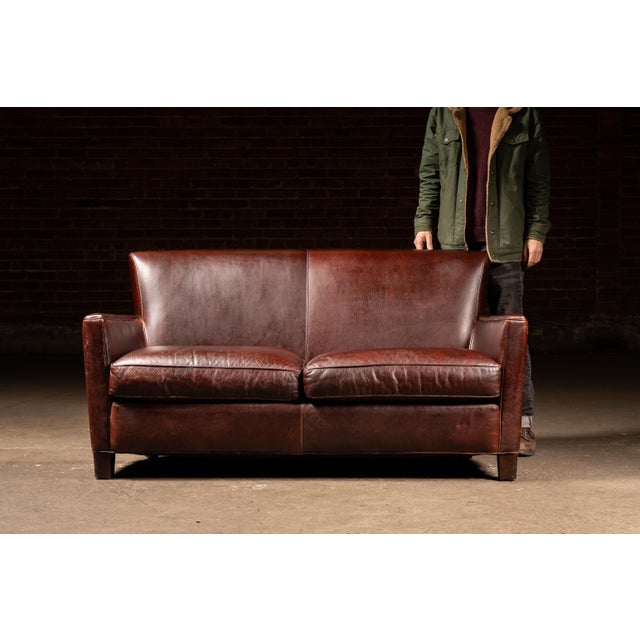 Low-slung two-seat sofa upholstered in rich brown leather with a restrained, architectural silhouette. The design leans...
