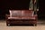 Low-slung two-seat sofa upholstered in rich brown leather with a restrained, architectural silhouette. The design leans...