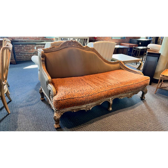 Large ornate chaise sofa in an umber color cushion. The wooden frame is set in a silver and gold like paint. The style has...