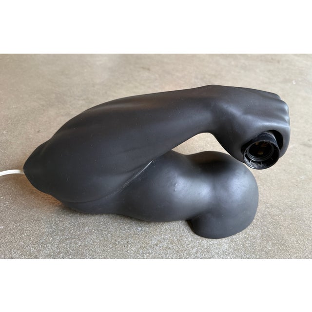 A striking pair of sculptural wall sconces featuring stylized arms grasping exposed globe bulbs, finished in a deep matte...