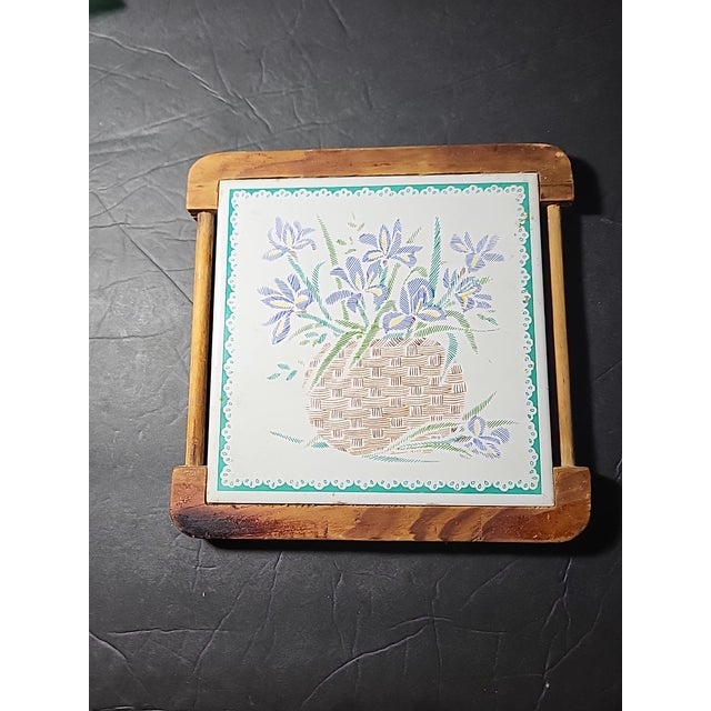 Vintage trivet made by Orient wrapped in an oak wood frame. The art is of a beautiful basket full of wild iris.