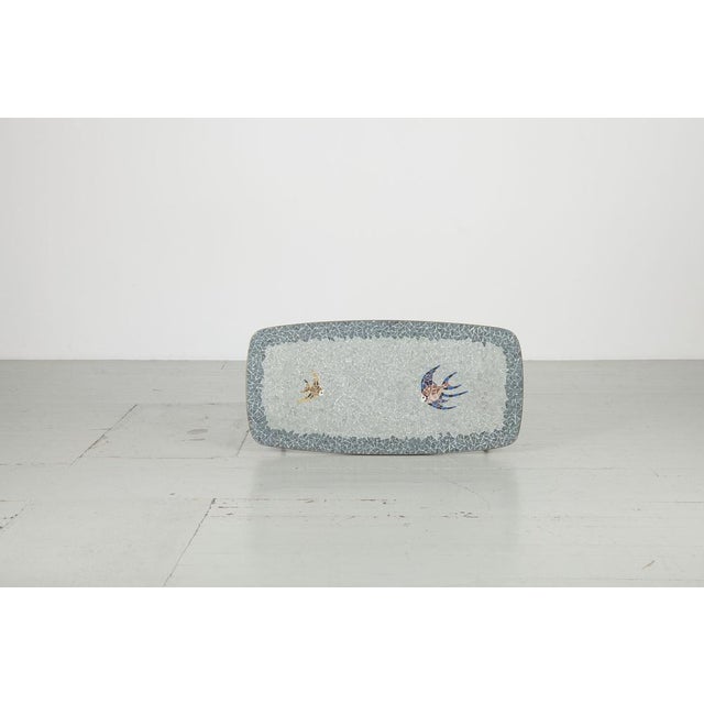 Supplement table with fish motif made of glass mosaic in bright pastel tones, 1950s. The border and the table legs are...