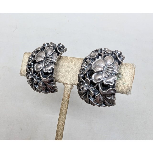 1970s silvertone floral half hoop clip back earrings. Marked "Napier." Measure: 1 1/16 inches long by 11/16 inches wide....