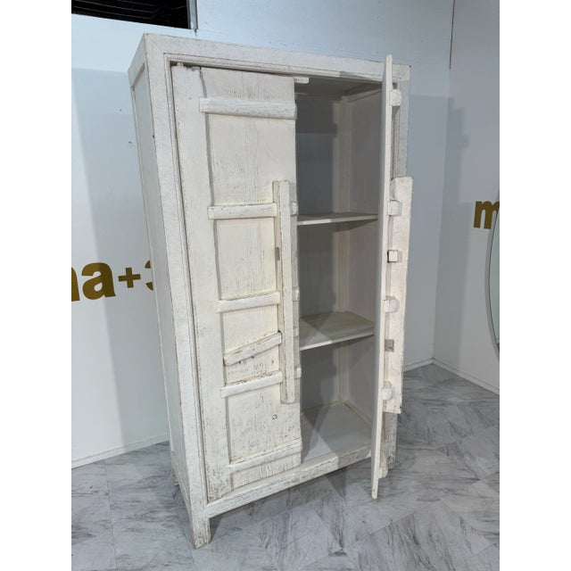 Charming vintage wooden armoire with a distressed whitewashed finish, showcasing bold geometric relief detailing on the...