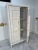Charming vintage wooden armoire with a distressed whitewashed finish, showcasing bold geometric relief detailing on the...