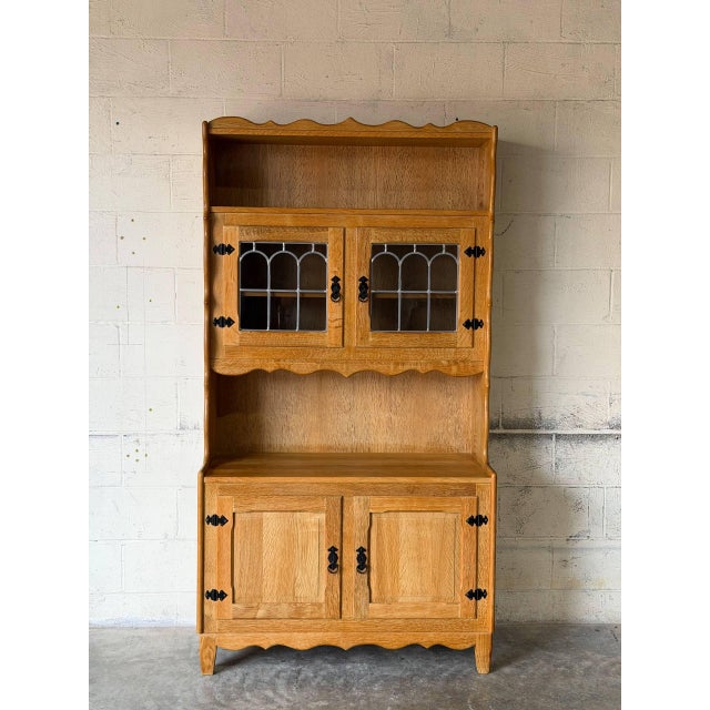 This striking oak hutch features upper glass doors with leaded details, open display shelving, and an enclosed lower...