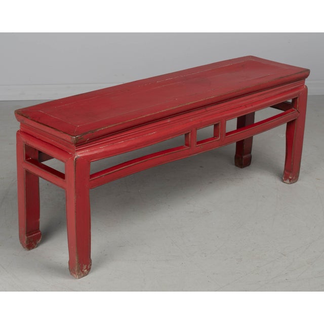 A 19th Century Chinese Qing dynasty red lacquered elm wood bench. Handcrafted using pegged and tenon construction with...