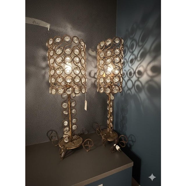 Elegant pair of Italian gilded metal table lamps featuring intricate scrollwork bases and sparkling crystal shades. These...