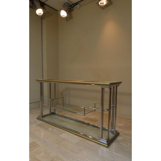 A vintage console table in the Hollywood Regency style, reminiscent of Maison Jansen\. it features a geometric frame made...