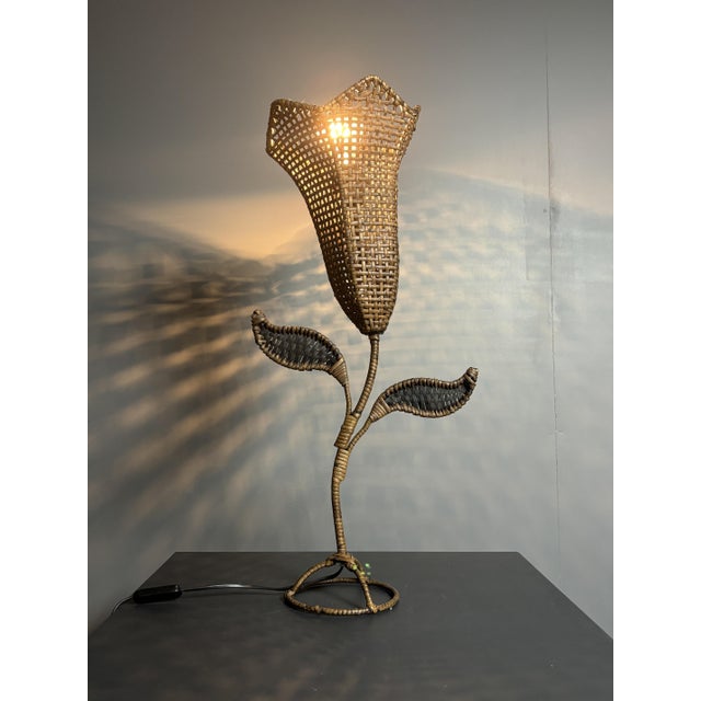 A sculptural table lamp in the form of a stylized tulip, entirely hand-woven in rattan and wicker over a wire armature....