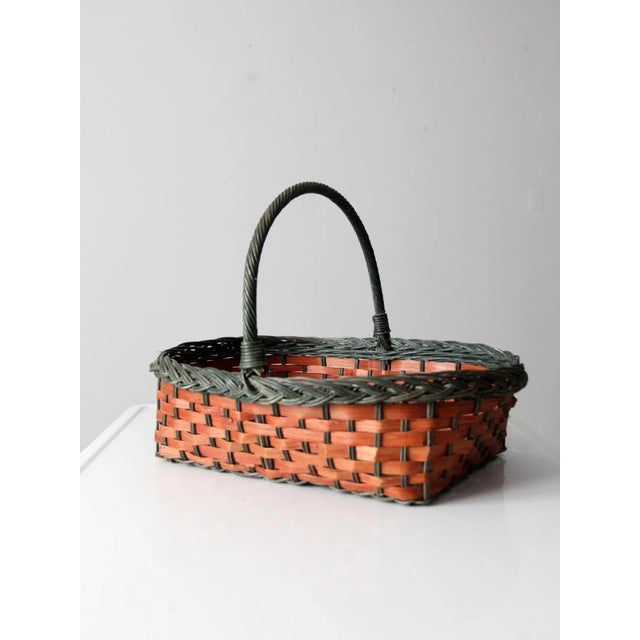 This is a vintage handle basket. The woven basket features a splint weave red body with green braided trim and handle. A...