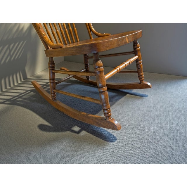 Beautiful vintage wooden rocking chair featuring a classic Windsor-inspired design with a detailed pressed-back ornate...