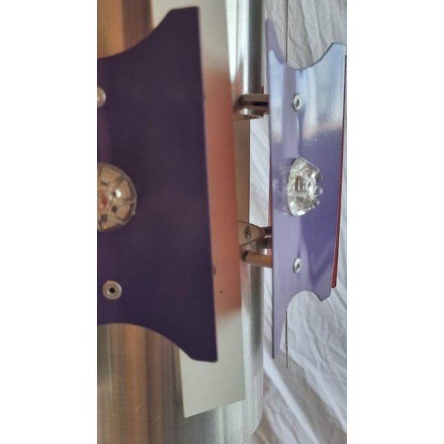 This pendant lamp is made of an iron tube and metal plates. The plates that are trapezium shaped are purple on the outside...