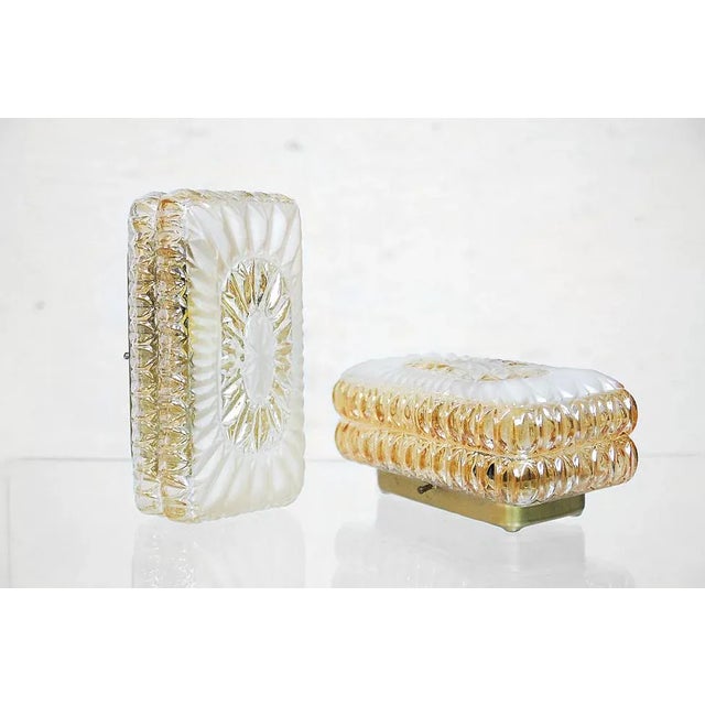 These modern wall sconces ware manufactured in the 1970s and are made from ice glass with a honey tint, sparkling in a...