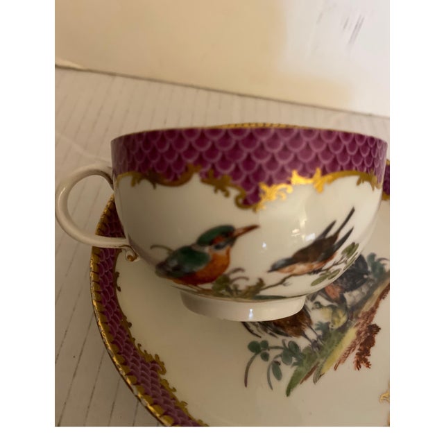 Diminutive whimsical 19th century Meissen cup and saucer. The purple trim with gilt decoration with birds and insects. The...