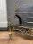 An English brass and wrought iron fire grate. The scrolled and shaped legs surmounted by finials, flanking a curved and...