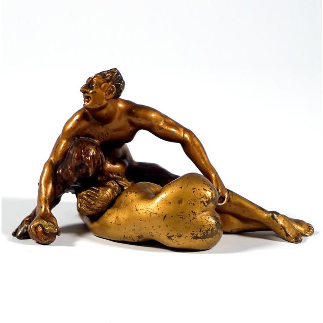 Crouching faun kneeling on one leg with outstretched arms, holding an apple in his right hand and looking to the side with...