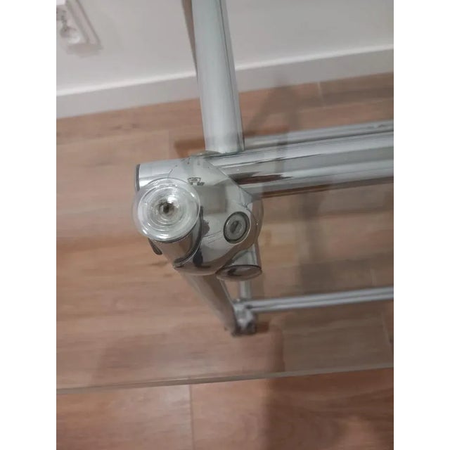 The table has a glass top and a glass shelf. The furniture has unique, massive joints of a metal structure (chrome-...