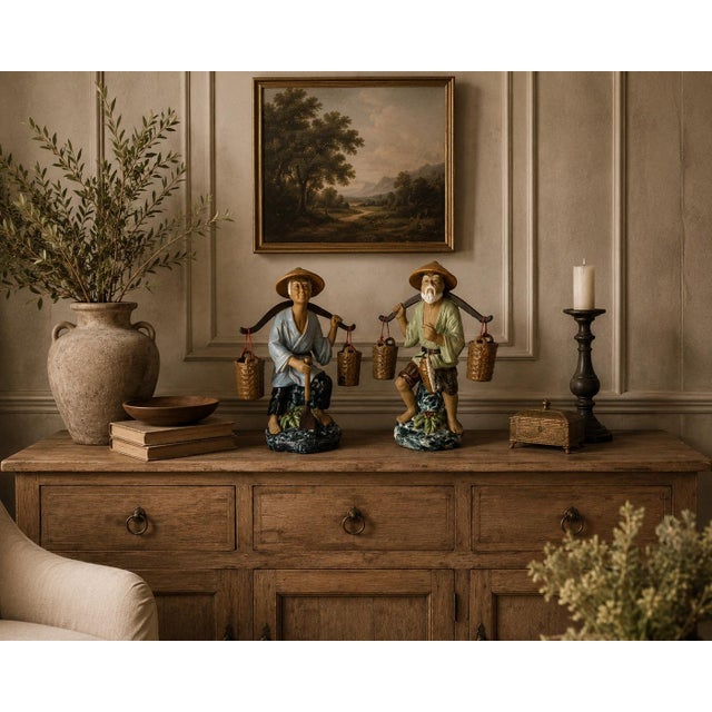 A charming pair of vintage Chinese ceramic figurines depicting rural farmers carrying traditional shoulder yokes with...