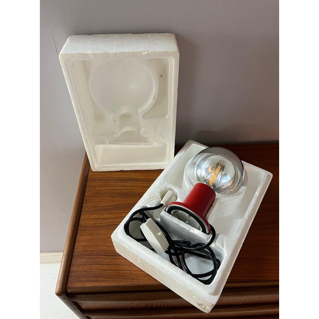 This table lamp consists of a red metal base and a screw-on glass globe shade. The shade is half transparent and half...