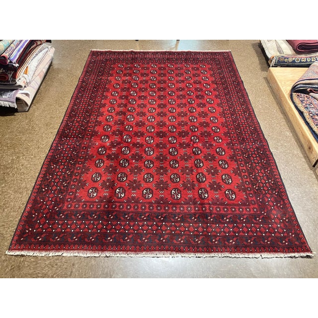 Vintage hand-knotted Afghan Bokhara rug with a red field covered in repeating elephant foot gul motifs and geometric...
