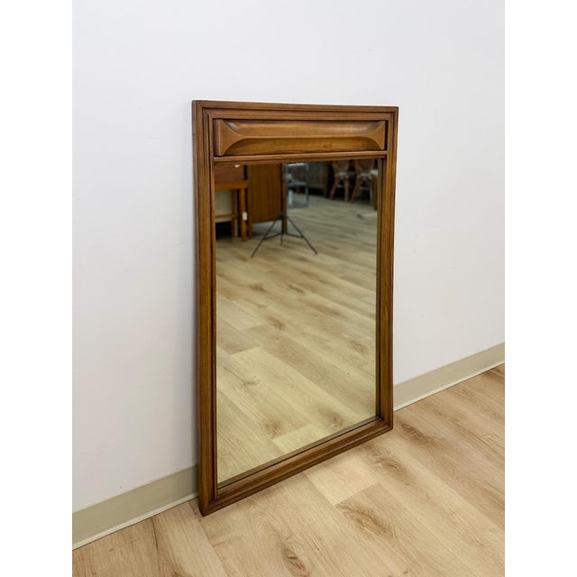 This vintage mid-century mirror features a rich walnut-toned wood frame with distinctive bowtie inlay detailing at the...
