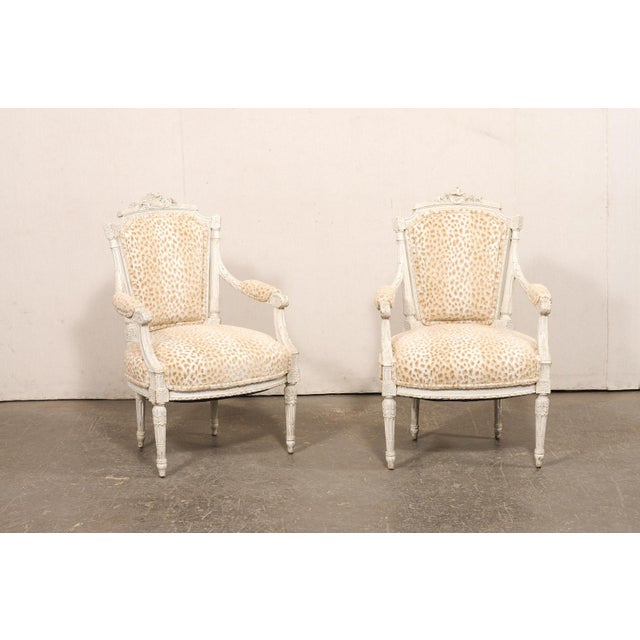 A French pair of Louis XVI style, carved-wood and upholstered armchairs from the 19th century. This antique pair of...