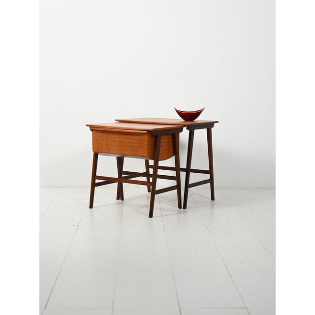 Two nesting coffee tables in dark lacquered oak with mahogany tops; one includes a sewing basket with a drawer. A 1950s...