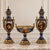 Elegant three-piece French-style porcelain garniture set featuring two matching covered vases and a coordinating central...
