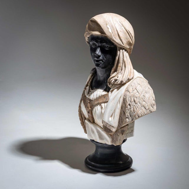 Life-size bust of a dark-skinned man with a headdress and light-coloured clothing. The bust is made of different types of...