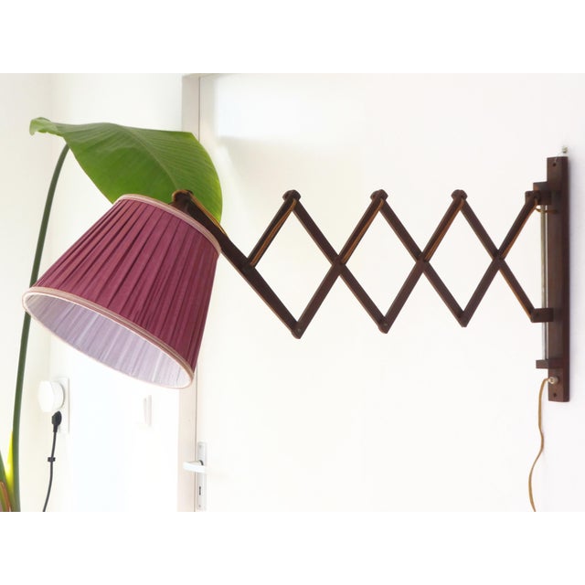 A mid century accordion style lamp with a wooden base and a fabric pleaded shade in red colour. The base is made out of...