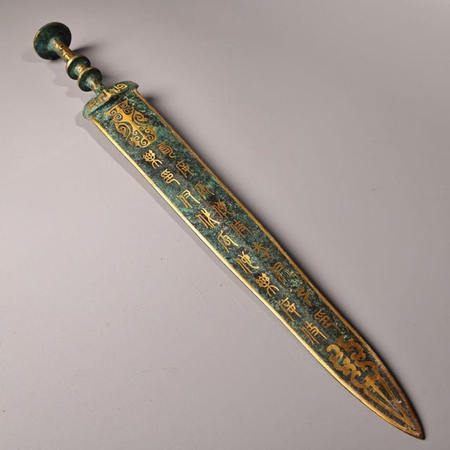 This is a cast bronze ceremonial dagger or short sword, featuring extensive gold inlay (gilt bronze) decoration. The blade...