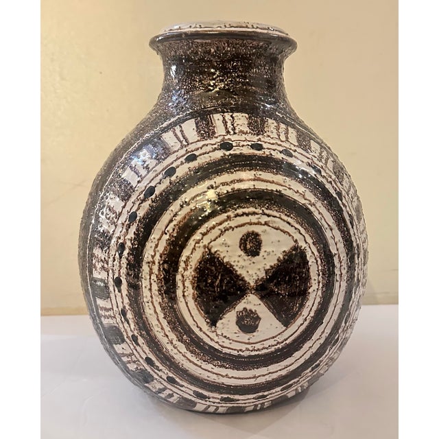 A round, bottle-shaped vessel with a short flared neck, wrapped in bold concentric rings that spiral out toward a central...