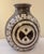 A round, bottle-shaped vessel with a short flared neck, wrapped in bold concentric rings that spiral out toward a central...