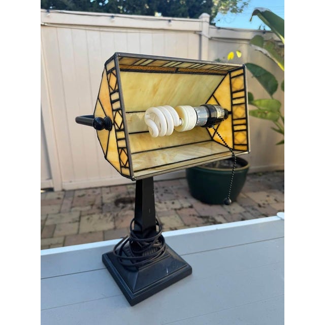 This vintage stained glass banker lamp features a rectangular shade in warm cream and amber tones with geometric...
